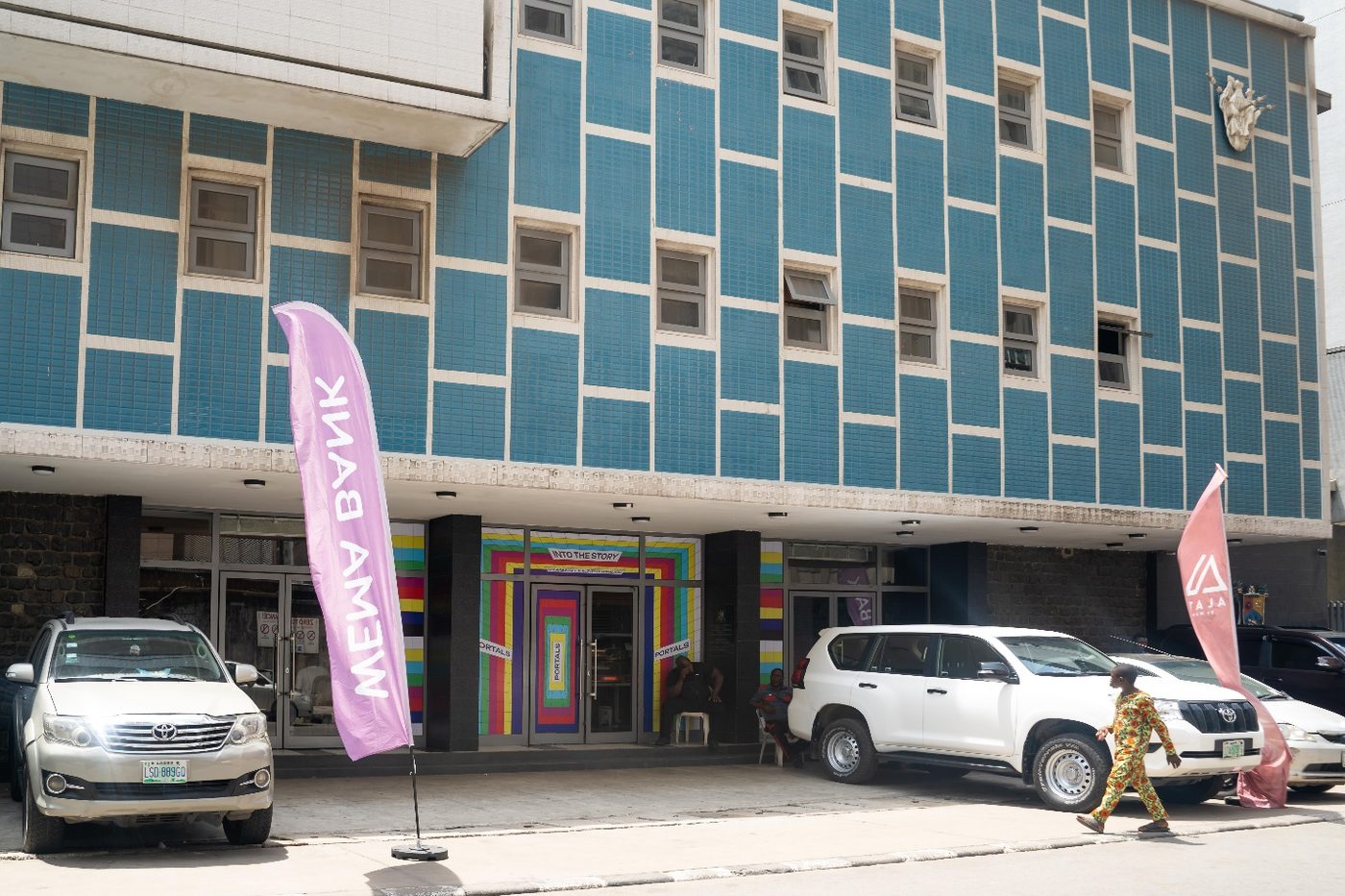 Glover Memorial Hall in daylight from Customs Street — the blue-tiled façade, the coloured entrance doors, and event banners on the forecourt.